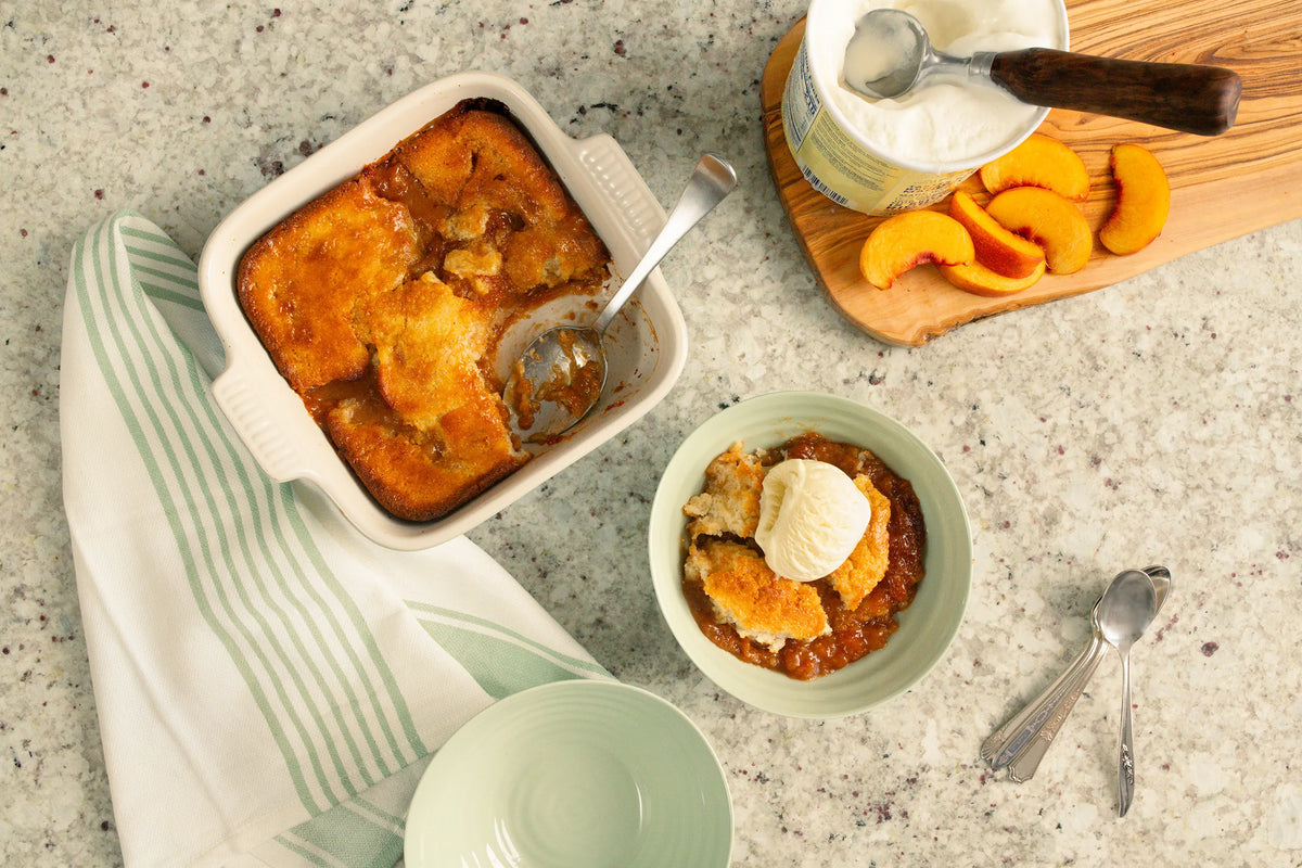 Peach cobbler in pan with spoon and bowl with peach cobber topped with ice cream