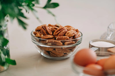 Glass bowl of pecans on a kitchen counter with eggs and a measuring cup in the foreground.